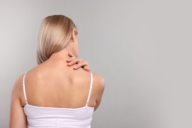 Photo of Woman suffering from pain in her neck on grey background, back view. Space for text