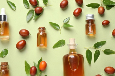 Glass bottles with jojoba oil and seeds on green background, flat lay