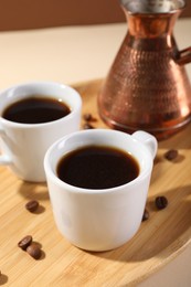 Photo of Delicious coffee in cups and beans on beige table, closeup