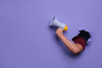 Special promotion. Man holding megaphone through hole in purple paper, closeup. Space for text