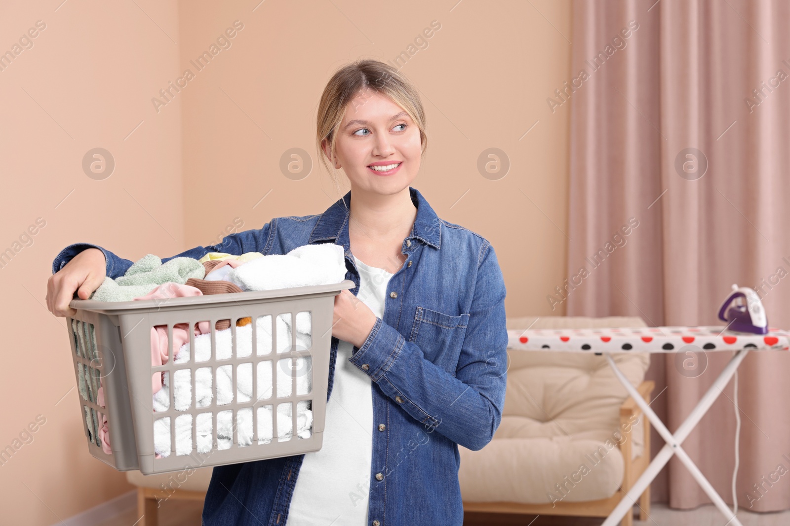 Photo of Happy woman with basket full of laundry at home