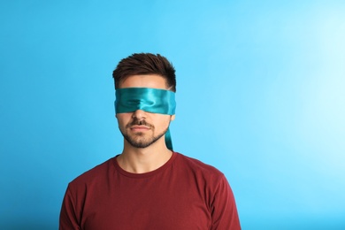 Young man with blindfold on blue background, space for text