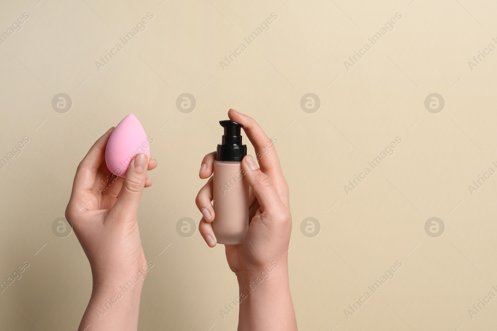 Photo of Woman holding bottle with skin foundation and makeup sponge on beige background, closeup. Space for text