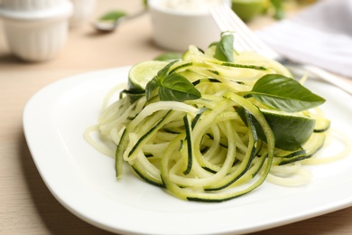 Photo of Tasty zucchini pasta with basil and lime on table, closeup