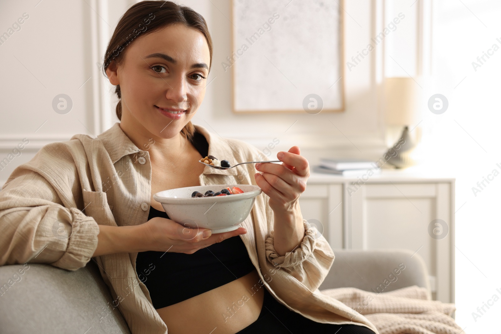Photo of Woman eating tasty granola with fresh berries and yogurt at home