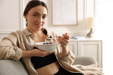 Photo of Woman eating tasty granola with fresh berries and yogurt at home