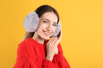 Happy woman wearing warm earmuffs on yellow background