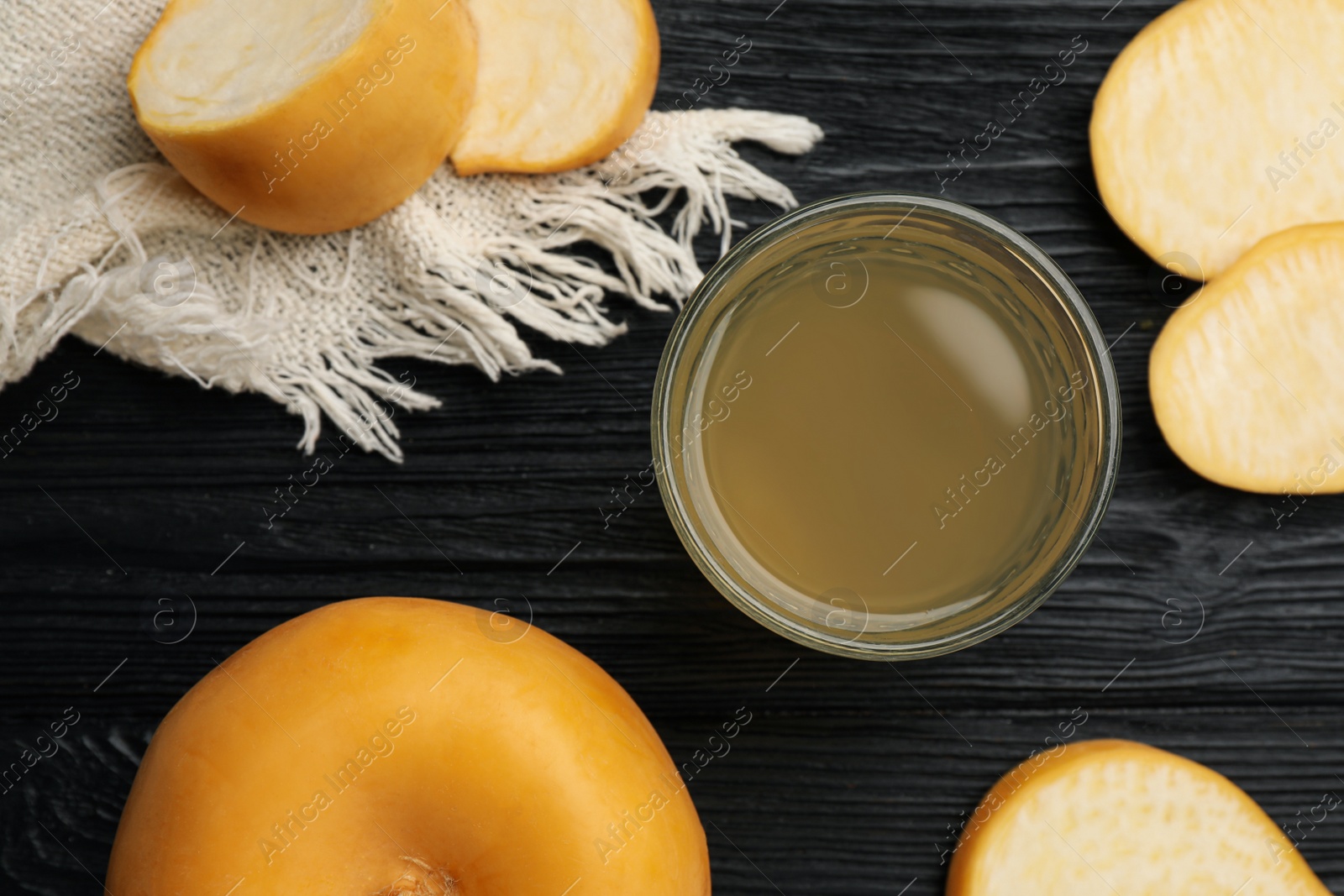 Photo of Glass of freshly made turnip juice on black wooden table, flat lay