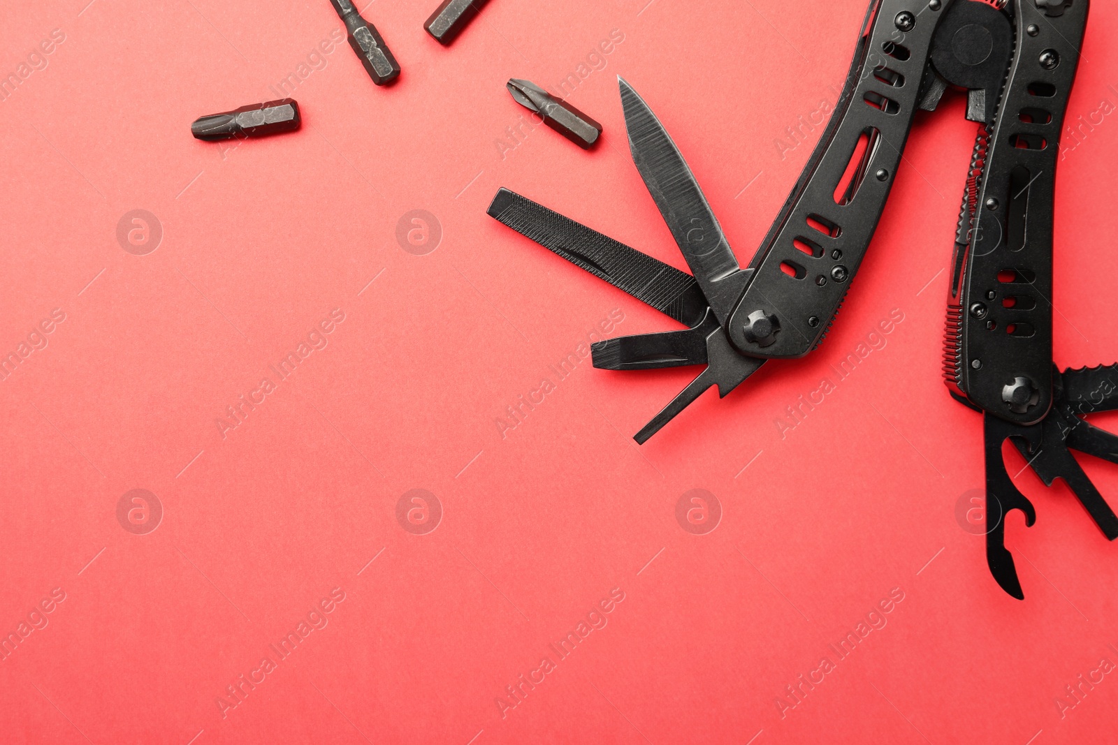 Photo of Compact portable black multitool and details on red background, flat lay. Space for text