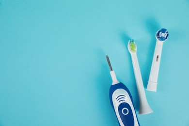Electric toothbrush and replacement brush heads on light blue background, flat lay. Space for text