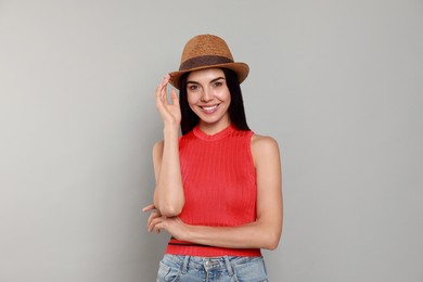 Beautiful young woman with straw hat on light grey background