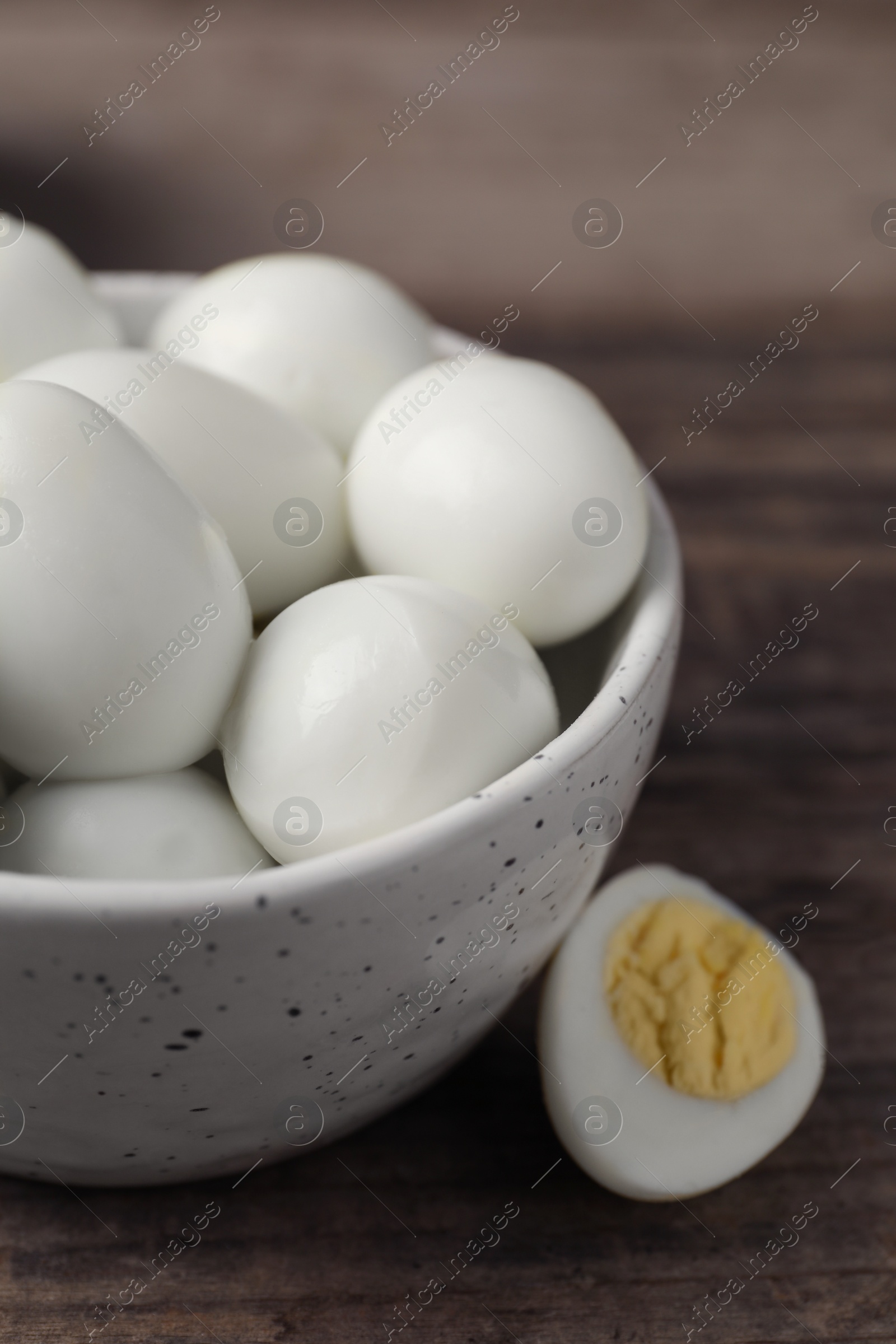 Photo of Many peeled hard boiled quail eggs in bowl on wooden table, closeup