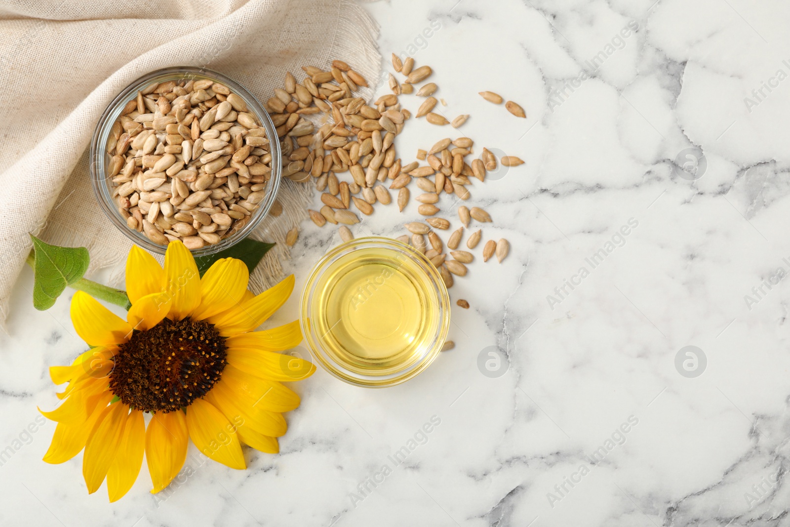 Photo of Sunflower, oil and seeds on white marble table, flat lay. Space for text