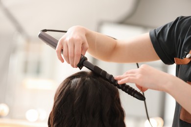 Photo of Hair styling. Hairdresser curling woman's hair in salon, closeup