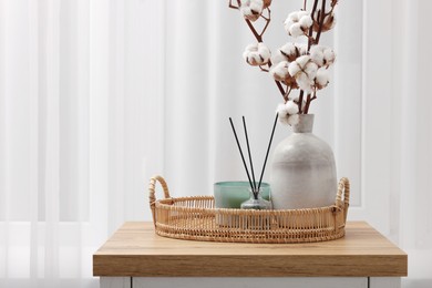 Photo of Candle, reed diffuser and vase with cotton branches on wooden commode indoors. Space for text