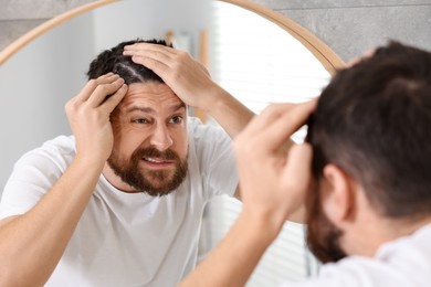 Photo of Emotional man with dandruff in his dark hair near mirror indoors