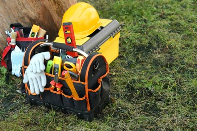 Bag, belt and box with different tools for repair on grass near tree outdoors, space for text