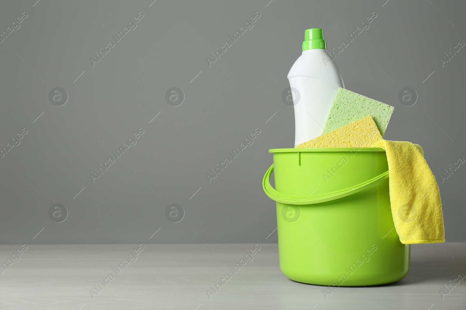 Photo of Bucket with cleaning products and sponges on grey table. Space for text