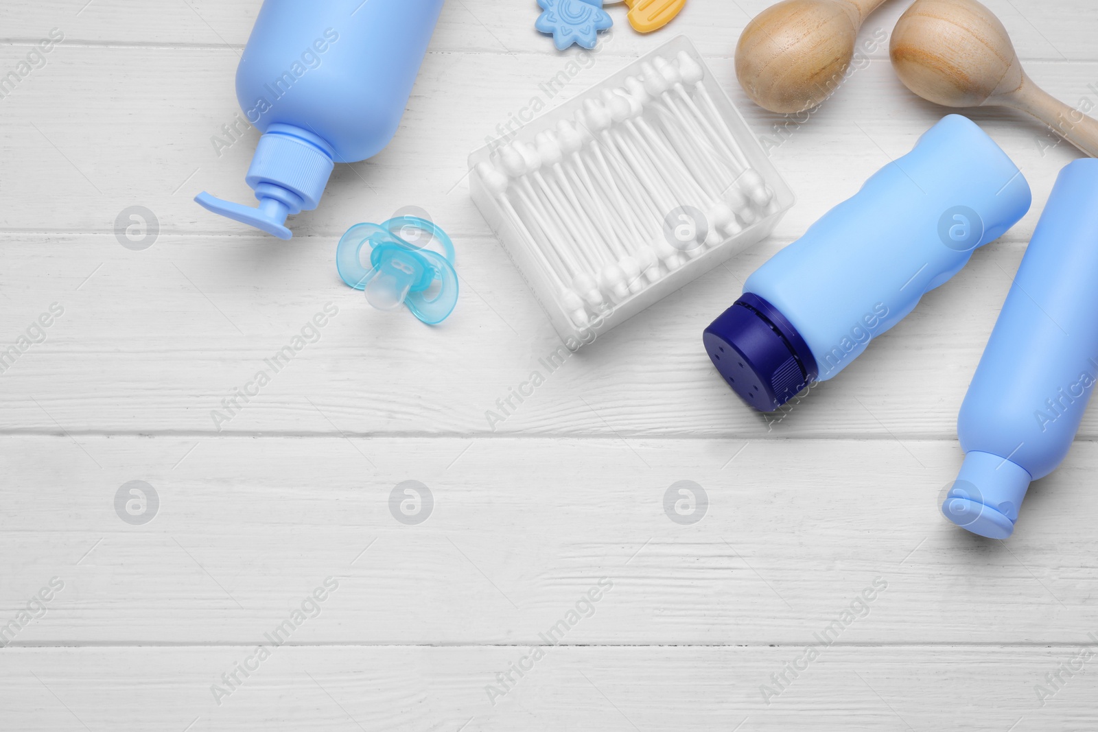 Photo of Baby powder, shampoo, pacifier, cotton buds and toys on white wooden table, flat lay. Space for text