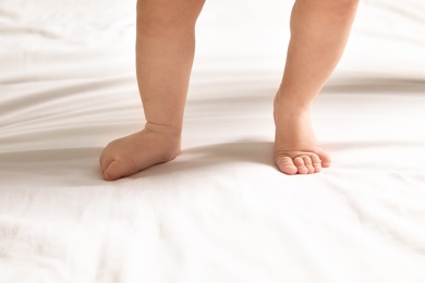 Photo of Cute little baby standing on white bed sheet, closeup