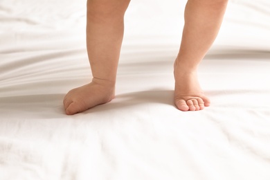 Cute little baby standing on white bed sheet, closeup