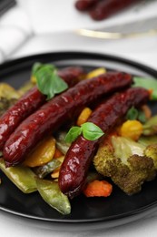 Photo of Delicious smoked sausages and baked vegetables on black plate, closeup