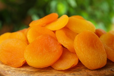 Photo of Tasty apricots on wooden board against blurred green background. Dried fruits