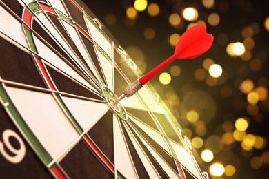 Image of Dart board with red arrow hitting target against blurred background, bokeh effect
