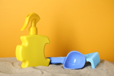 Suntan product and plastic beach toys on sand against yellow background