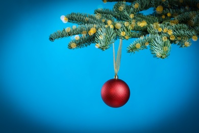 Beautiful Christmas ball hanging on fir tree branch against light blue background, bokeh effect. Space for text