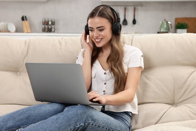 Happy woman with headphones and laptop on couch in room