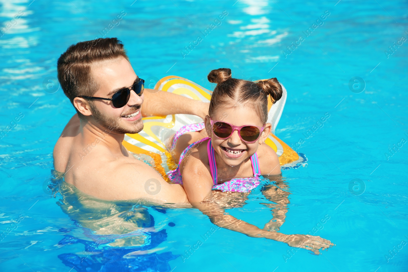 Photo of Father teaching daughter to swim with inflatable star in pool on sunny day