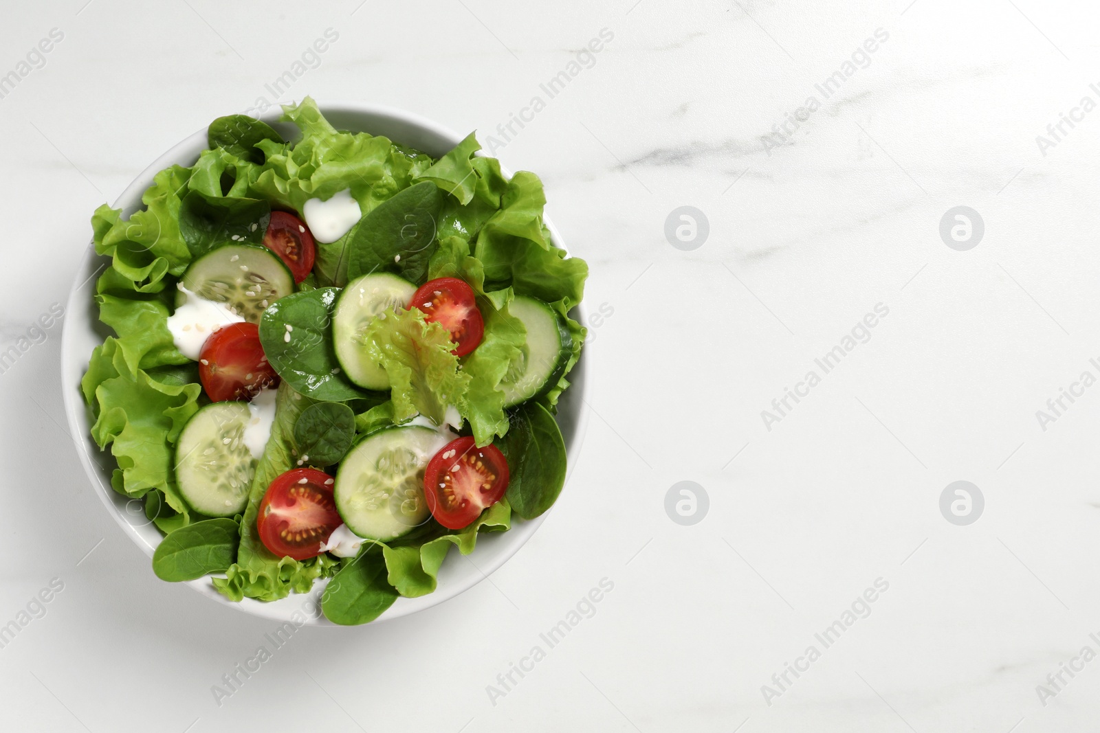 Photo of Delicious salad in bowl on white marble table, top view. Space for text