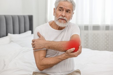 Senior man suffering from pain in elbow on bed at home