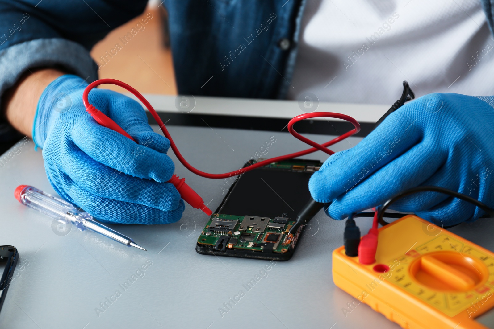 Photo of Technician checking broken smartphone at table in repair shop, closeup