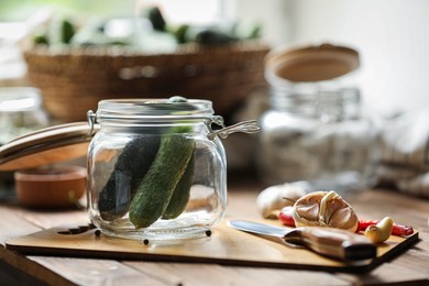 Glass jar with fresh cucumbers and other ingredients on wooden table, space for text. Pickling vegetables