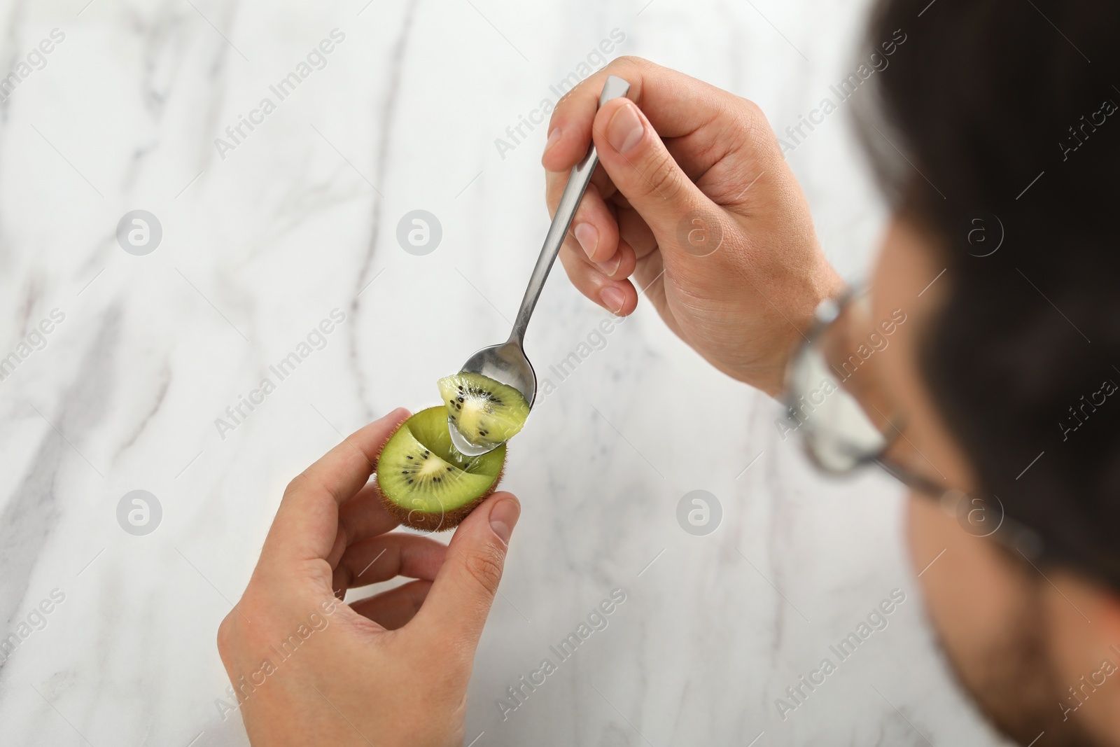 Photo of Man eating kiwi with spoon on blurred background, closeup