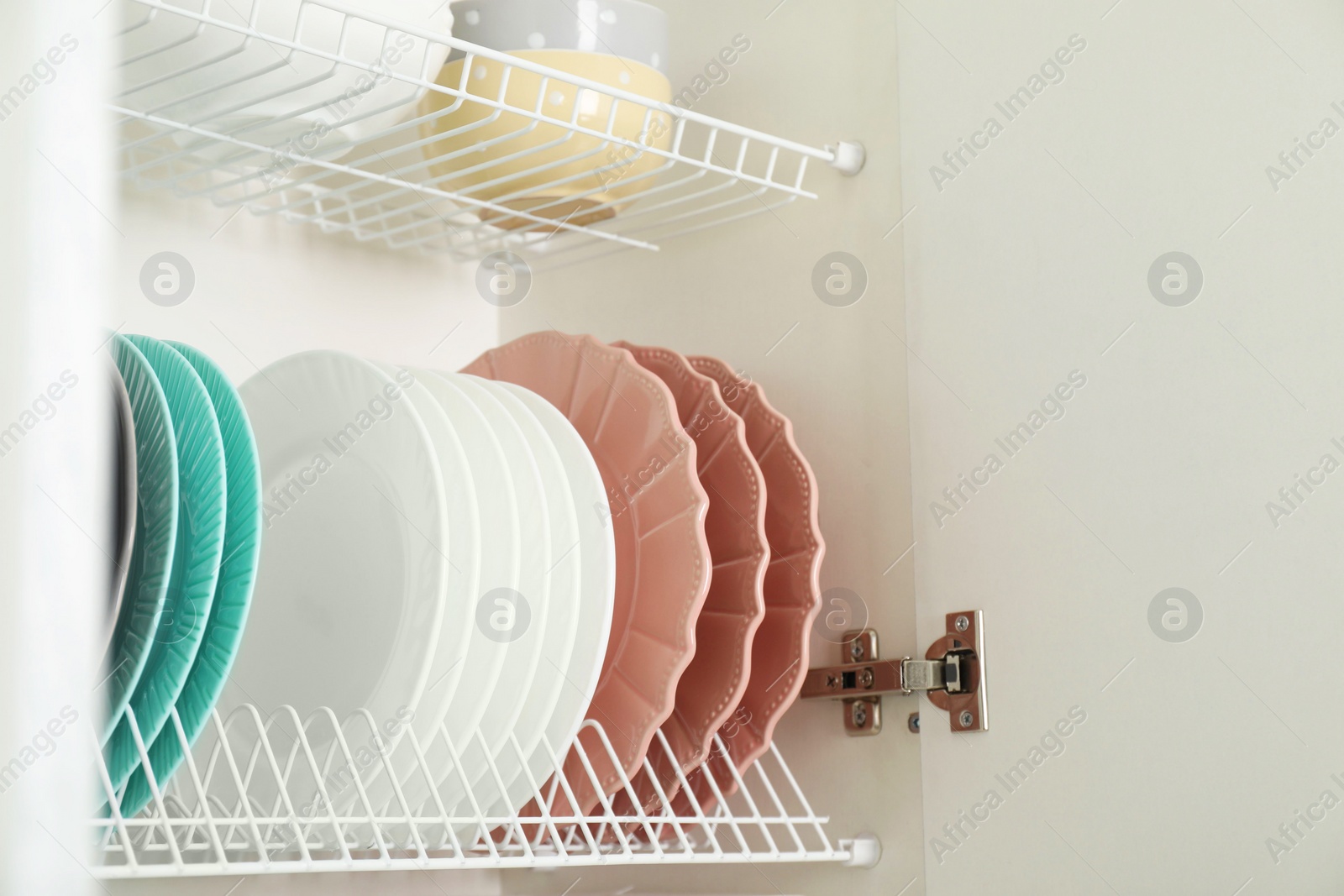 Photo of Clean plates and bowls on shelves in cabinet indoors