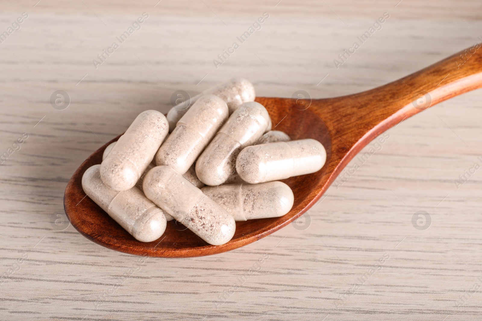 Photo of Spoon with gelatin capsules on wooden table, closeup