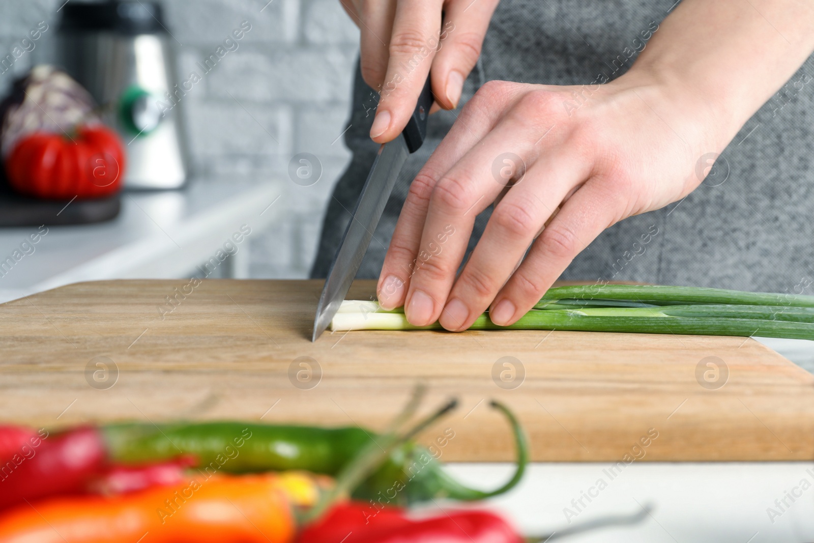 Photo of Woman cutting green spring onion on wooden board at white table, closeup