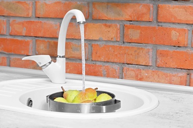 Fresh ripe pears under tap water in kitchen sink near brick wall