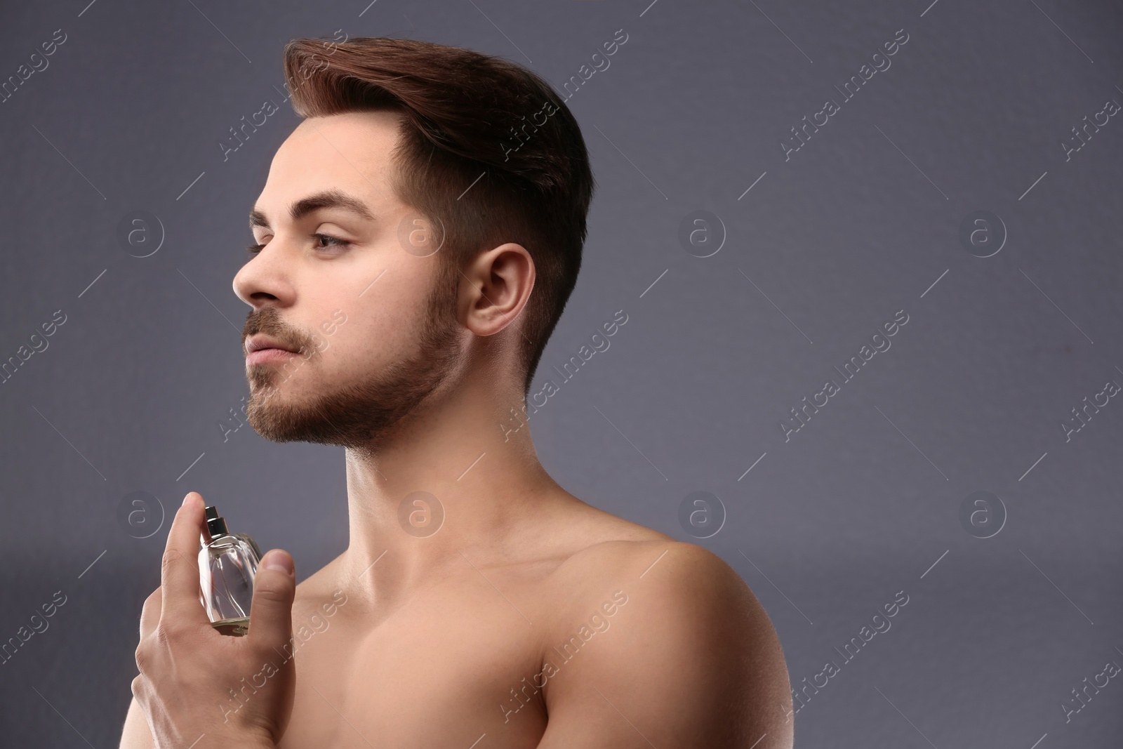 Photo of Handsome man using perfume on grey background