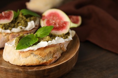 Tasty bruschettas with cream cheese, pesto sauce, figs and fresh basil on wooden table, closeup. Space for text