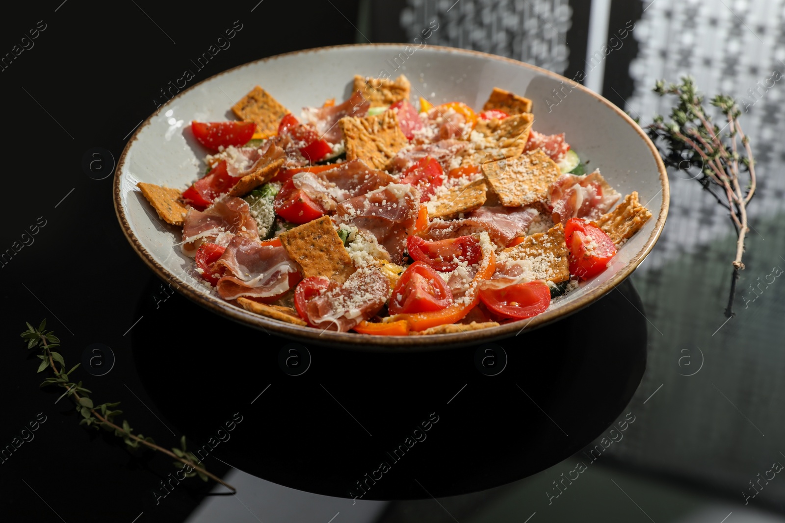 Photo of Beautiful composition of salad with prosciutto on black table in studio. Food stylist