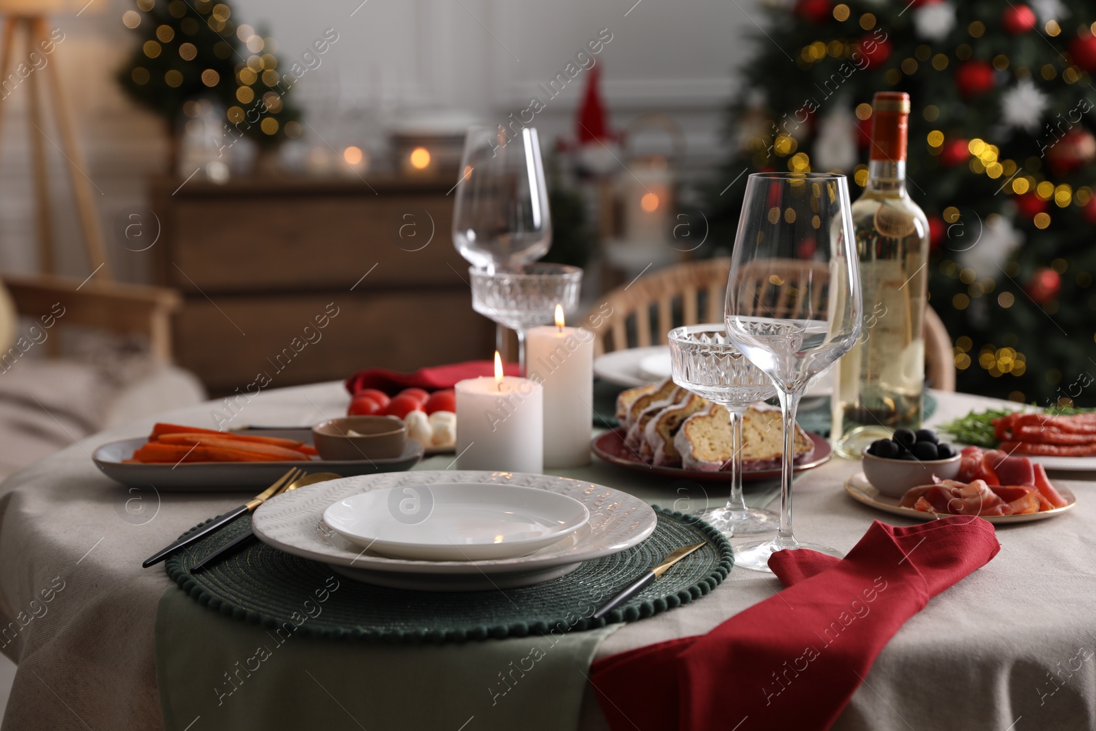 Photo of Christmas table setting with burning candles, appetizers and dishware indoors
