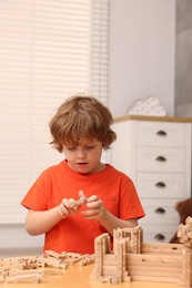 Little boy playing with wooden construction set at table in room. Child's toy