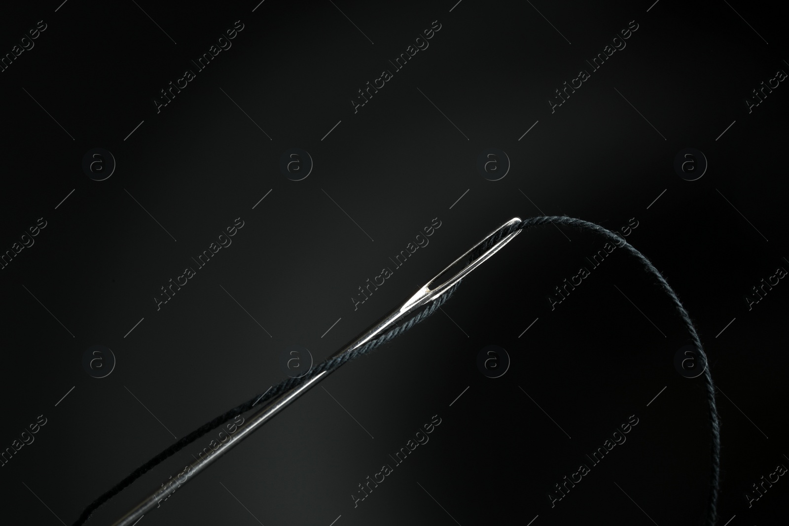 Photo of Sewing needle with black thread on dark background, closeup
