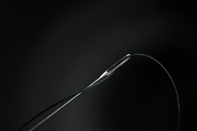 Sewing needle with black thread on dark background, closeup
