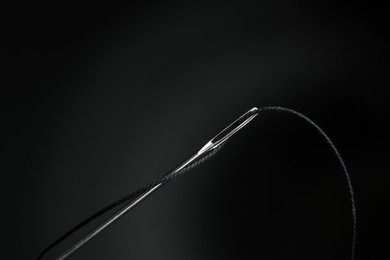 Photo of Sewing needle with black thread on dark background, closeup