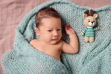 Photo of Cute newborn baby with toy deer in turquoise knitted blanket lying on bed, top view